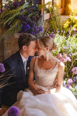 A romantic wedding couple share an intimate moment surrounded by purple flowers and greenery in golden sunlight at the Sunstone Winery.