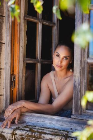 Woman in beige top leans on rustic wooden windowsill with green foliage framing the shot at the Sunstone Winery.