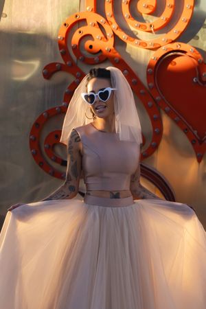 A rock 'n roll bride in retro heart sunglasses and a beige tulle dress poses in front of vintage Las Vegas sign at the Neon Museum.