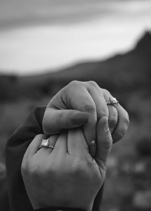 Black and white close-up photograph of two hands clasped together showing engagement or wedding rings.