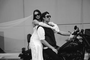 Black and white photo of two people posing on a motorcycle together wearing sunglasses and stylish attire.