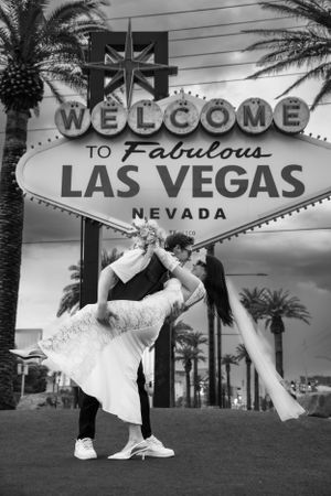 An elopement couple embraces in front of the iconic Welcome to Fabulous Las Vegas sign in black and white photography.