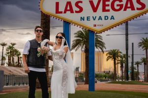 An elopement couple together at the iconic Welcome to Las Vegas sign with palm trees and city buildings in the background.