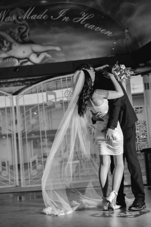A romantic black and white wedding photo showing a couple kissing under a sign reading Was Made in Heaven at the Little White Chapel.