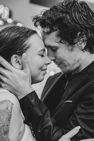 Black and white portrait of a bride and groom in a tender romantic moment with their eyes closed and foreheads touching in the rain.