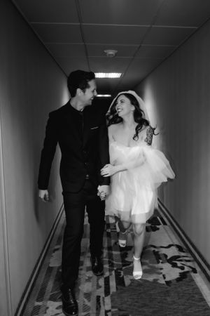 A Las Vegas elopement couple in black and white walking down a hotel hallway, with her in a white dress and him in a dark suit.
