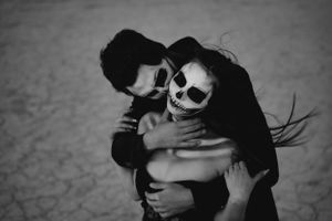 A monochromatic artistic portrait of two people embracing,  wearing dramatic skeleton-style face makeup.