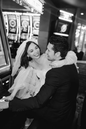 A black and white photo of newlyweds sharing a joyful moment in front of Las Vegas casino slot machines.