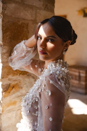 A bride poses in an elegant sheer wedding gown with delicate floral appliques in warm natural lighting.