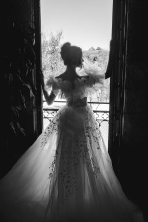 A silhouetted bride in an elegant wedding dress stands before open French doors in dramatic black and white at the Sunstone Winery.