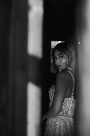 Dramatic black and white boudoir portrait of bride in an elegant sequined gown looking over their shoulder in moody lighting.