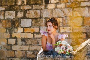 Beautiful bride in a pink wedding dress with elegant sunset lighting against rustic stone wall background.