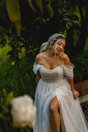 Ethereal off-shoulder white wedding dress with slit photographed in a southern California lush garden setting with soft natural lighting.
