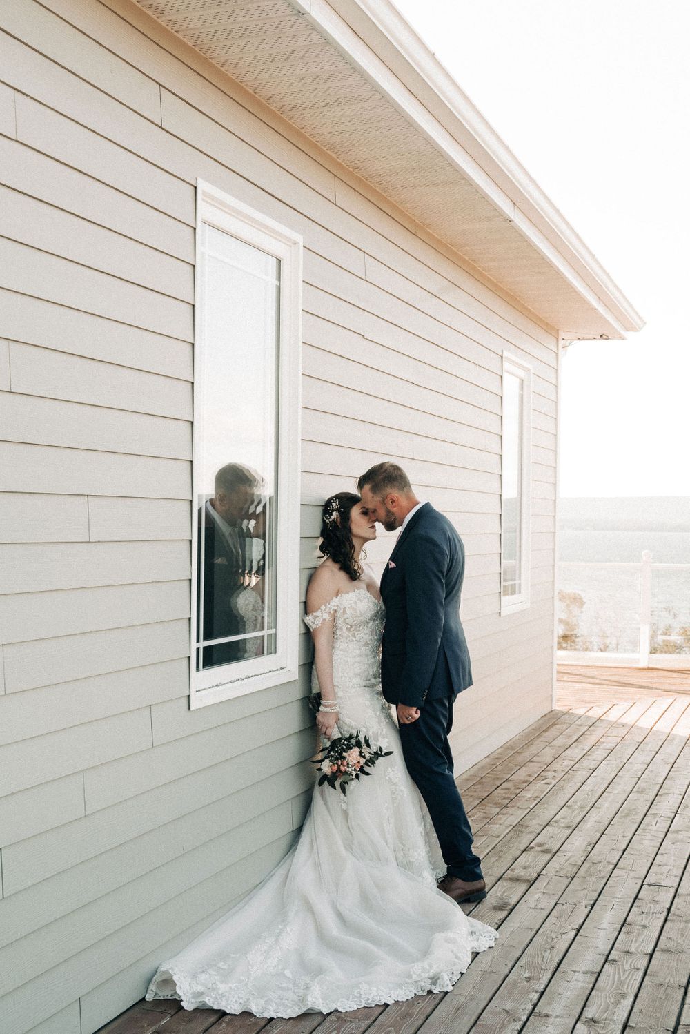 Wedding couple shares intimate moment against white clapboard house on deck.