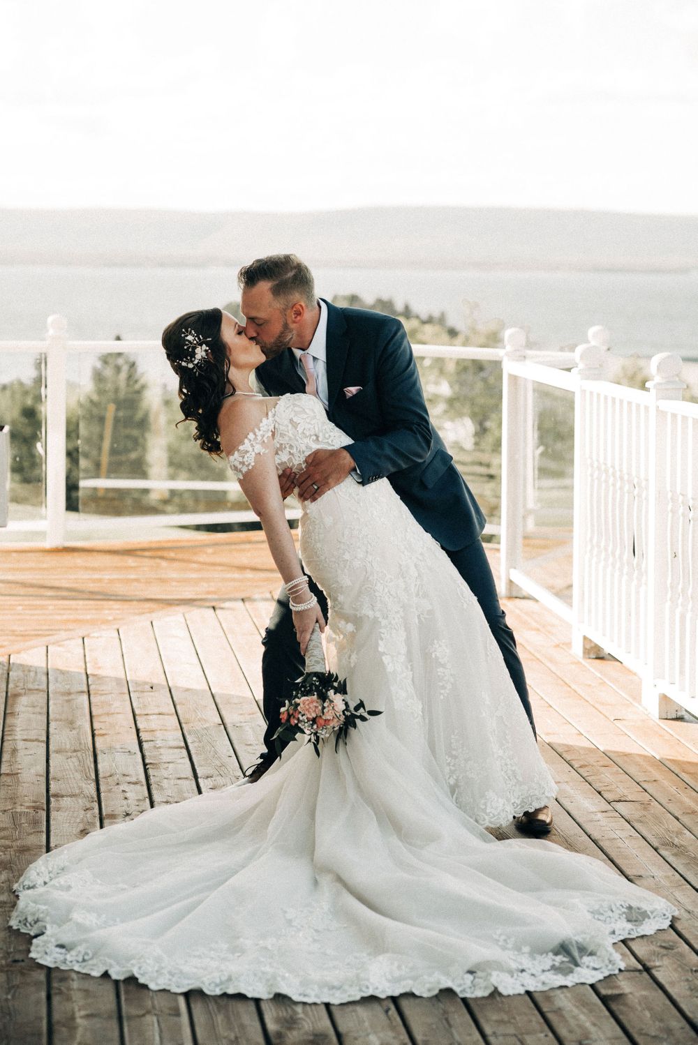 Classic wedding dip pose on deck showcasing detailed lace wedding gown.
