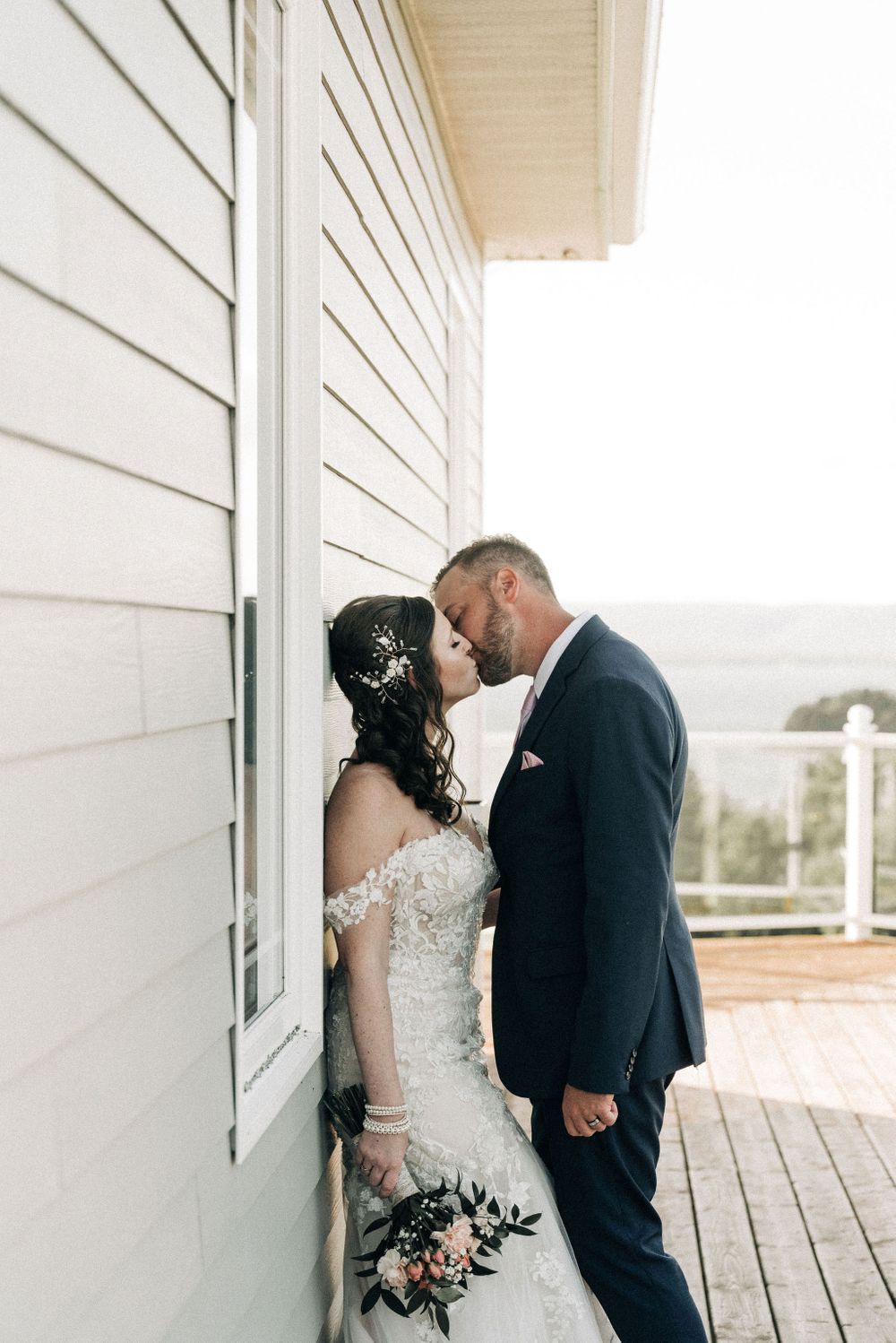 Romantic wedding moment captured against white siding of house.
