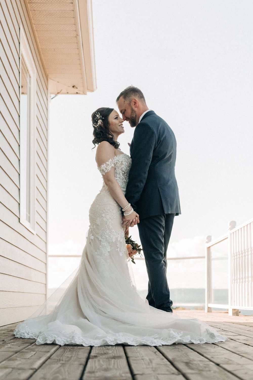 Elegant wedding portrait of couple in formal attire on wooden deck.