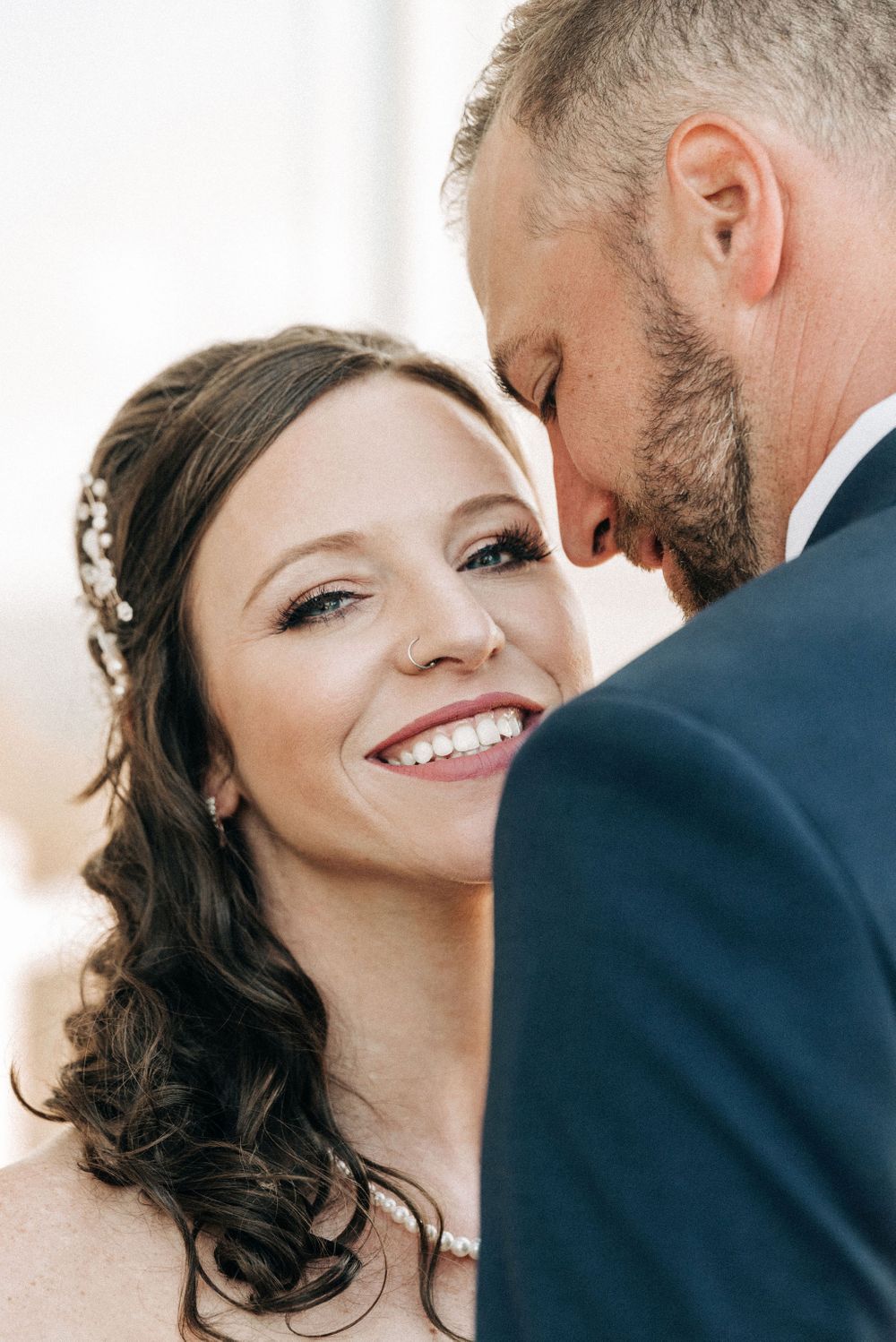 Intimate close-up wedding portrait showing bride's joyful smile and groom's tender moment.