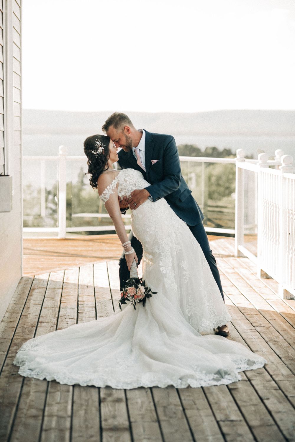 Dramatic wedding dip pose on wooden deck with stunning white lace dress trailing.