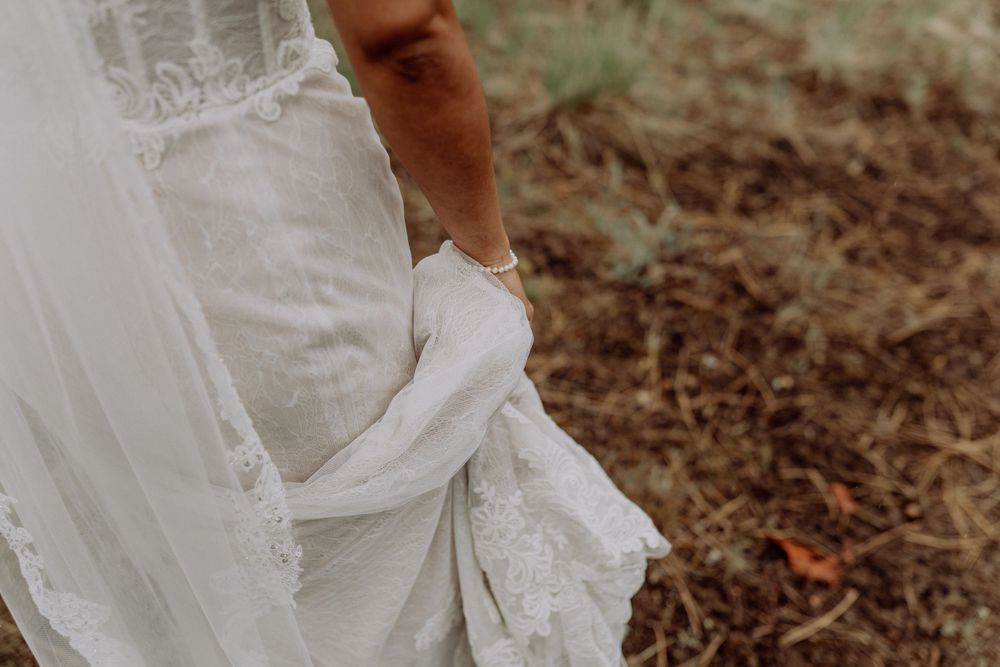 Detail shot of a white wedding dress hem being held on natural ground.