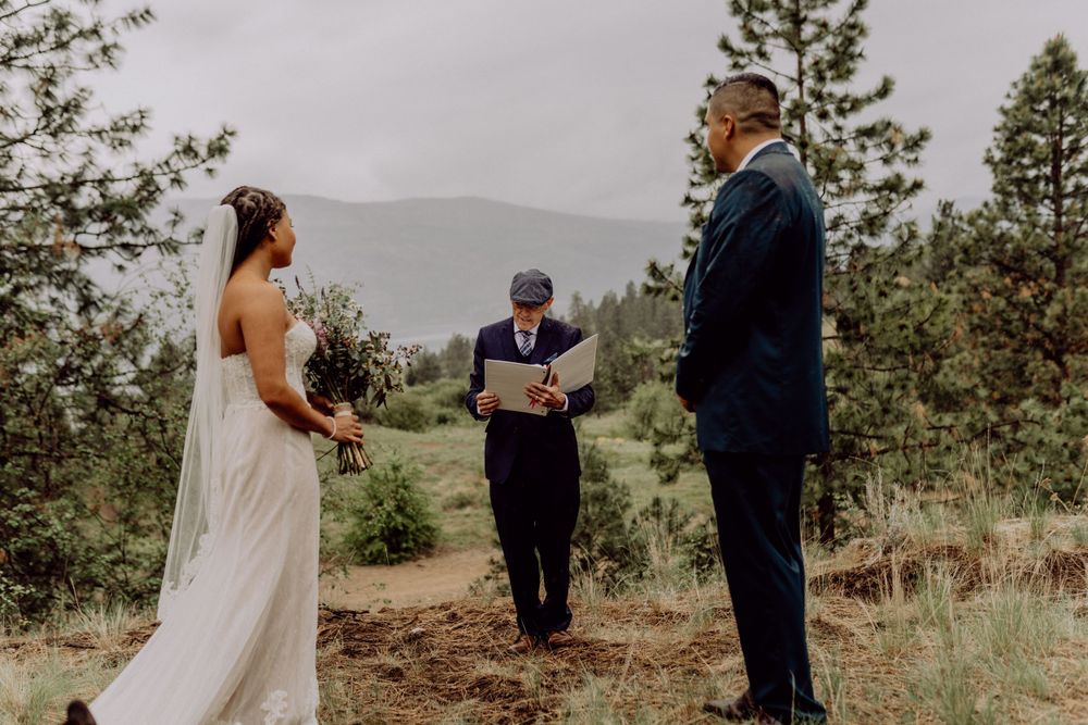 Outdoor wedding ceremony taking place on a hillside surrounded by pine trees.