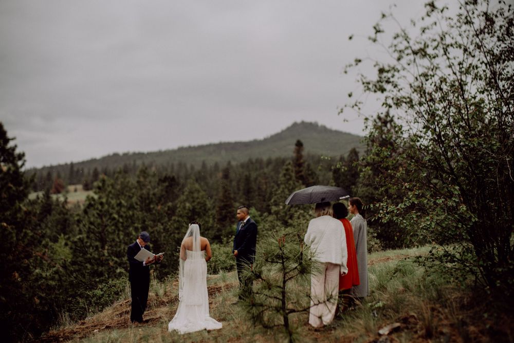 Wedding ceremony participants stand on a mountain slope under cloudy skies.