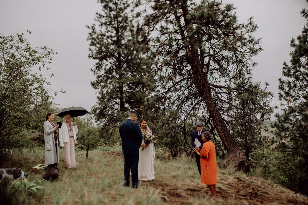 Small wedding group gathered on a hillside for an intimate ceremony under umbrellas.