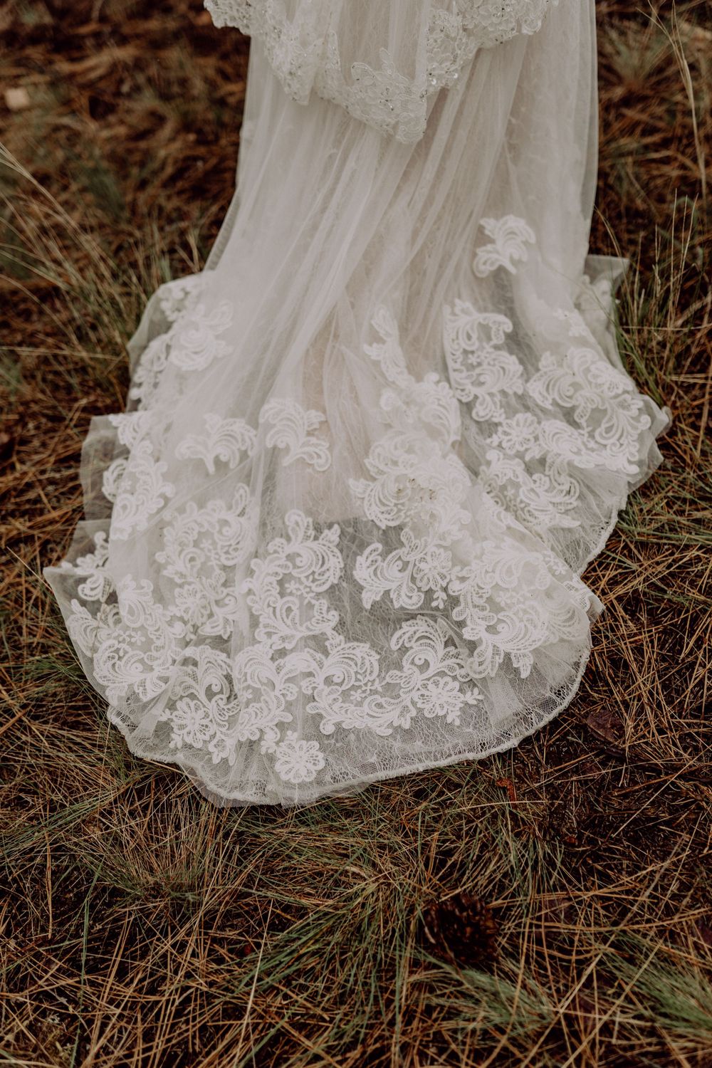 Detailed shot of intricate lace trim on a white wedding dress train against natural ground.