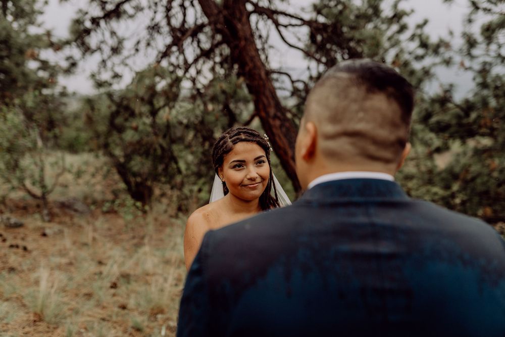Intimate wedding moment captured in rustic outdoor setting with pine trees.