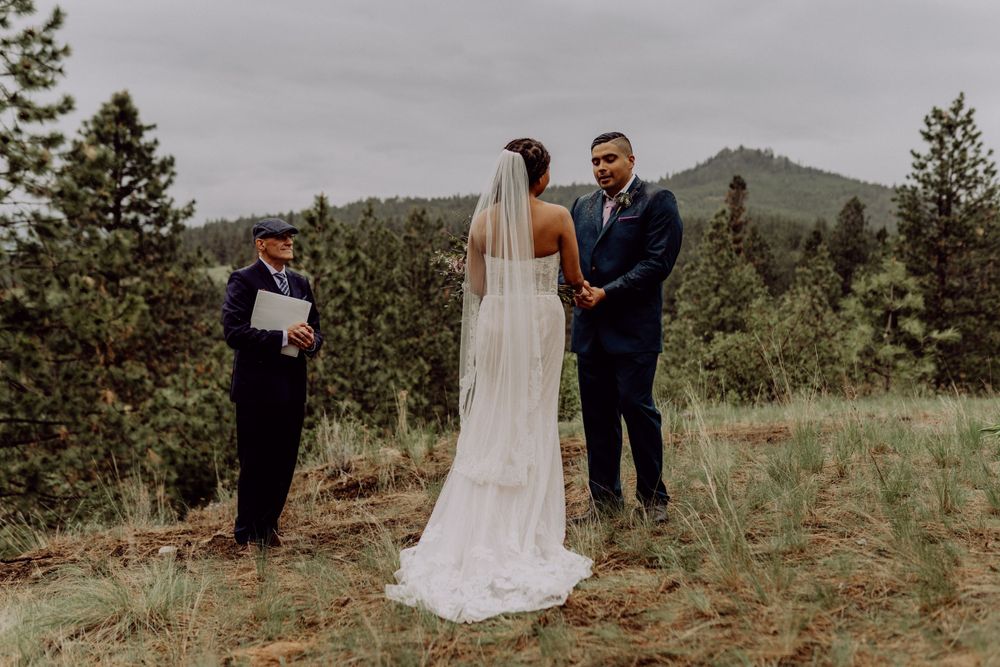 Wedding ceremony in mountain landscape with officiant and flowing white dress.