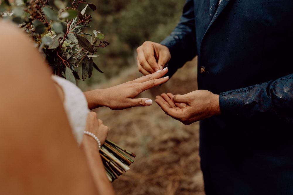 Close-up of ring exchange during outdoor wedding ceremony with rustic bouquet.