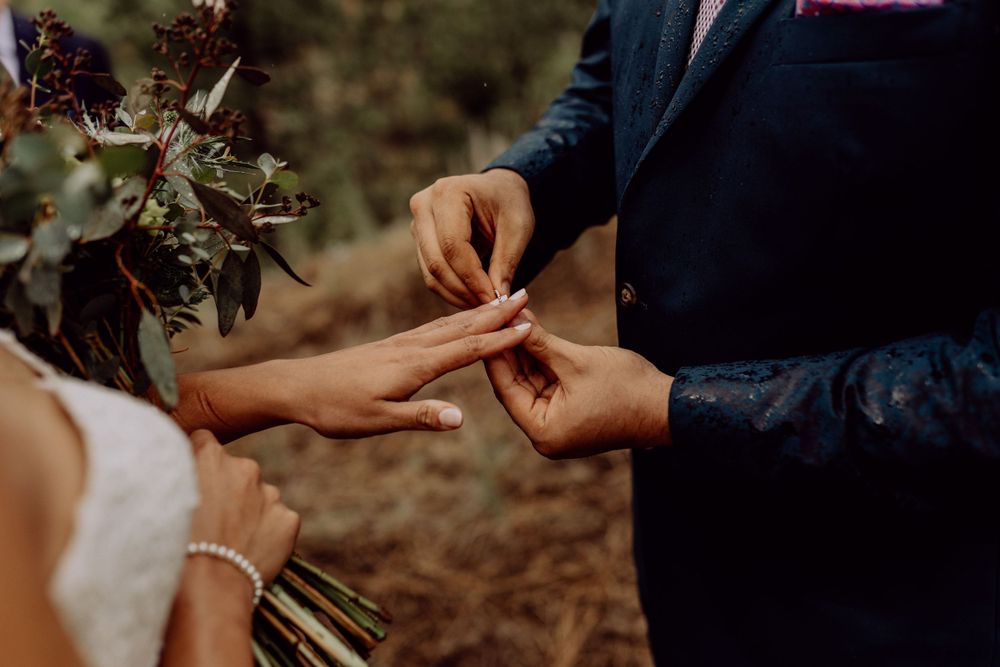 Detail shot of wedding ring exchange with floral bouquet during outdoor ceremony.