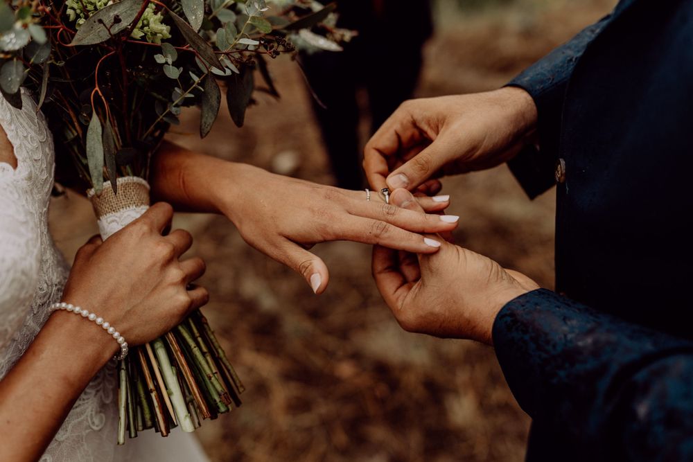 Close-up of hands exchanging wedding rings with a bridal bouquet in view.