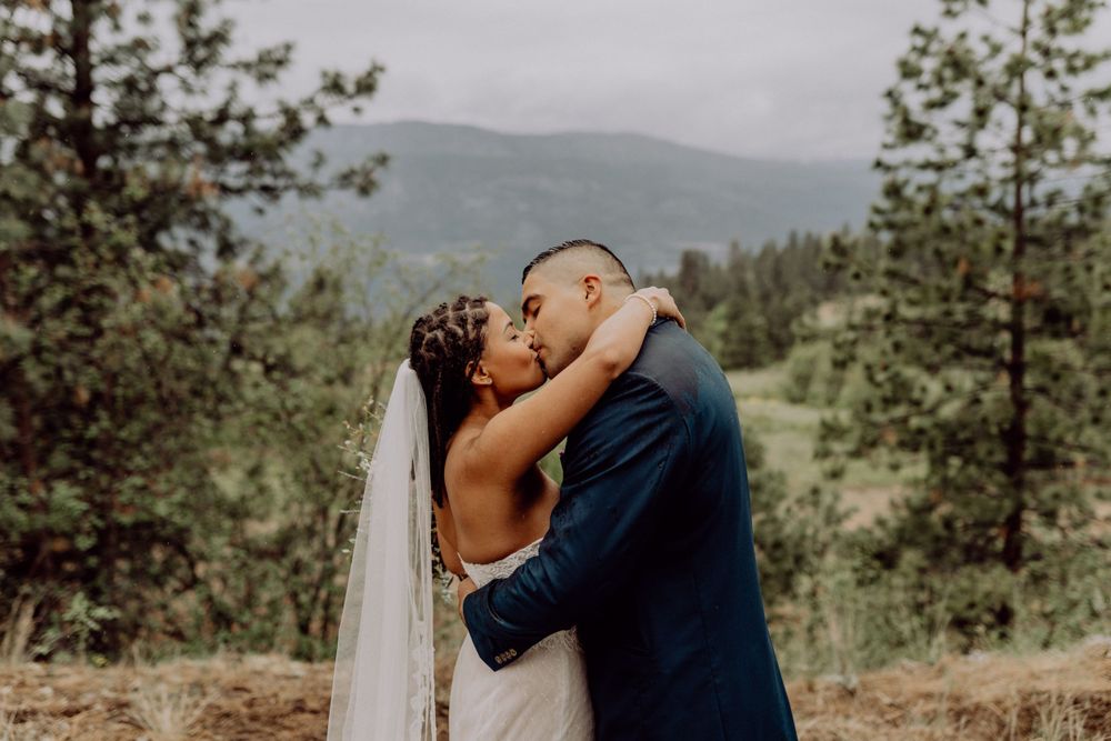 Newlyweds share a passionate kiss with scenic mountain views behind them.