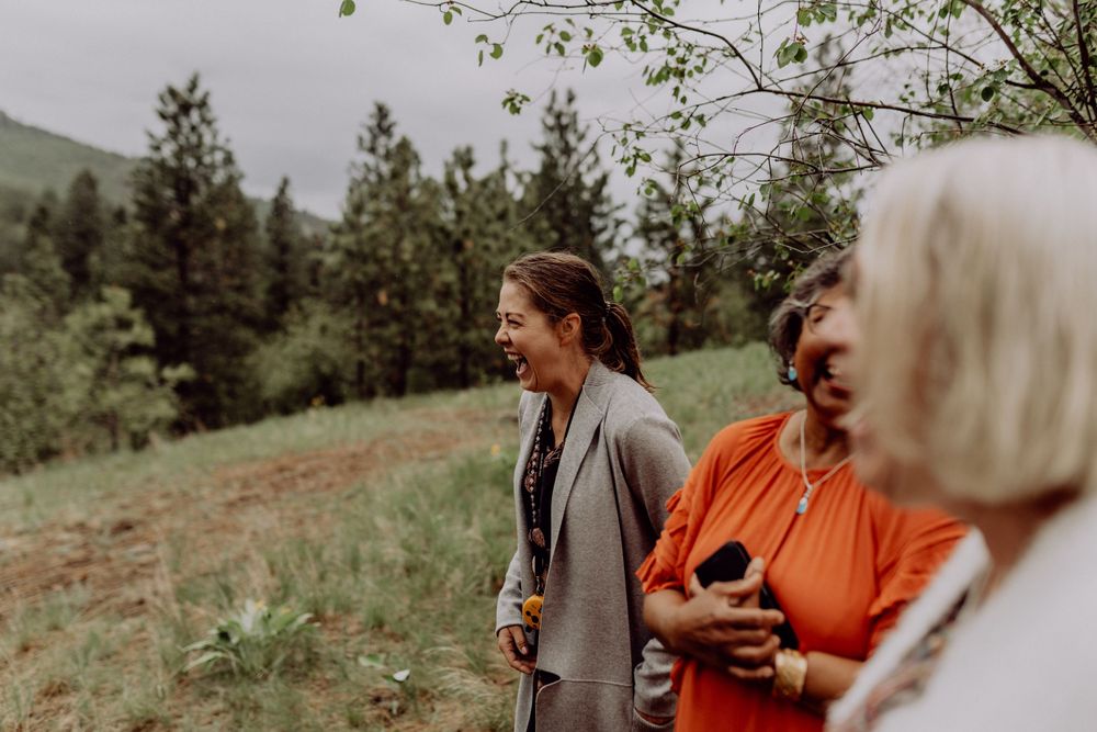 Wedding guests watch the ceremony on a mountainside with evergreen trees in the background.