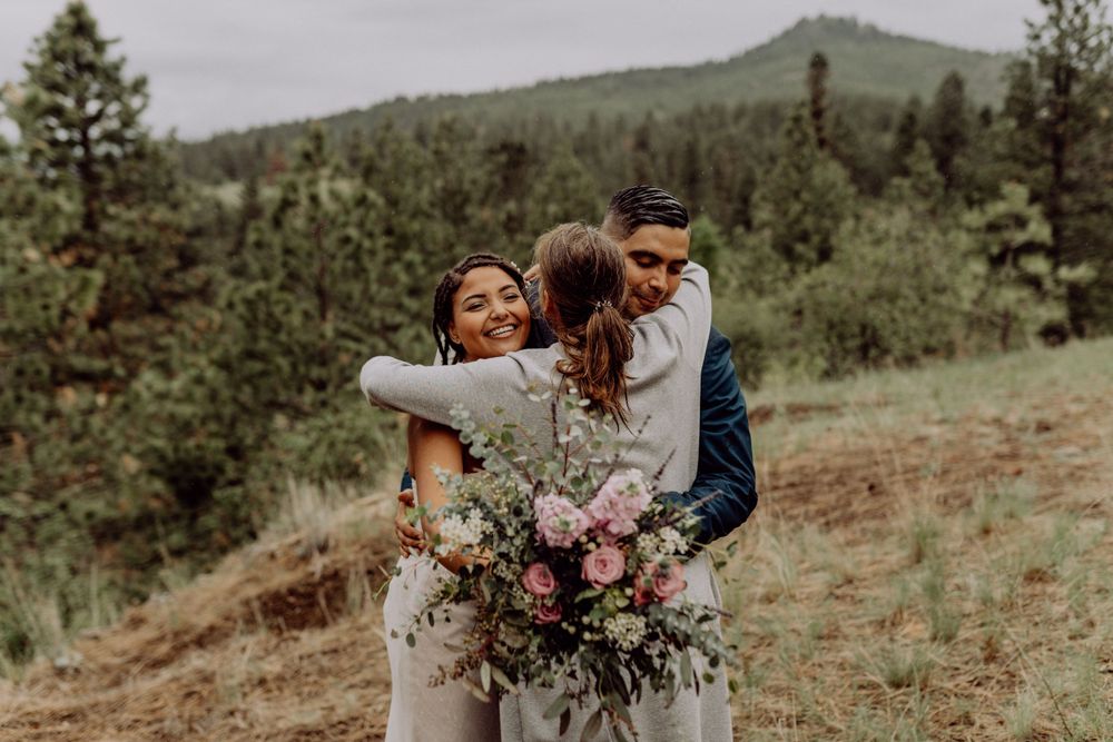 Joyful embrace between newlyweds with a large wedding bouquet on a mountain hillside.