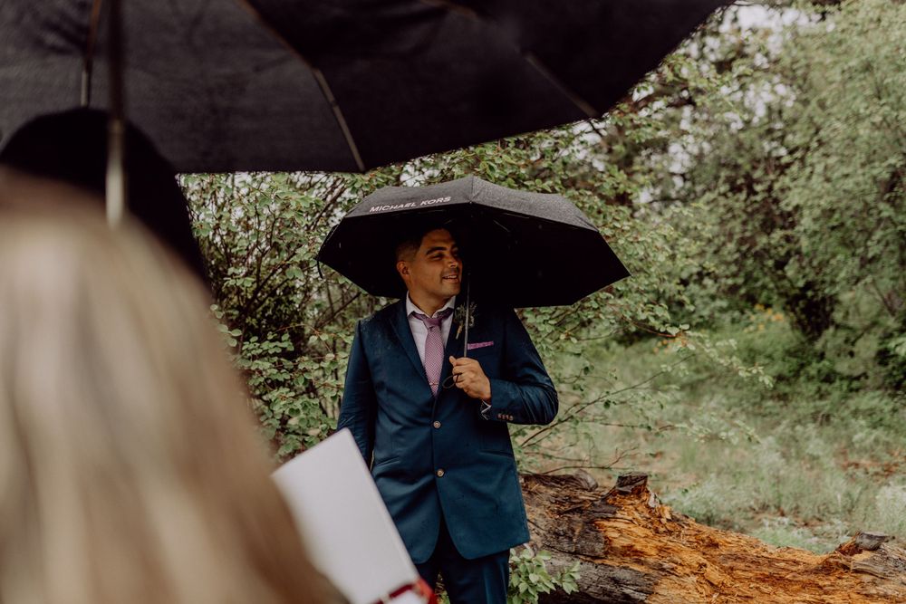 Figure holding black umbrella during outdoor ceremony in natural setting.