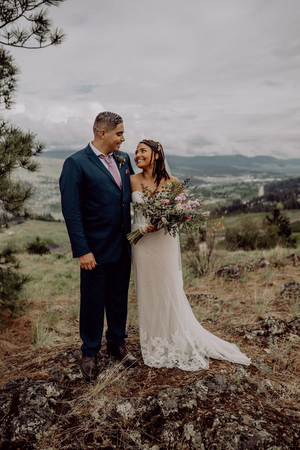 Wedding couple standing on rocky overlook with mountain views.