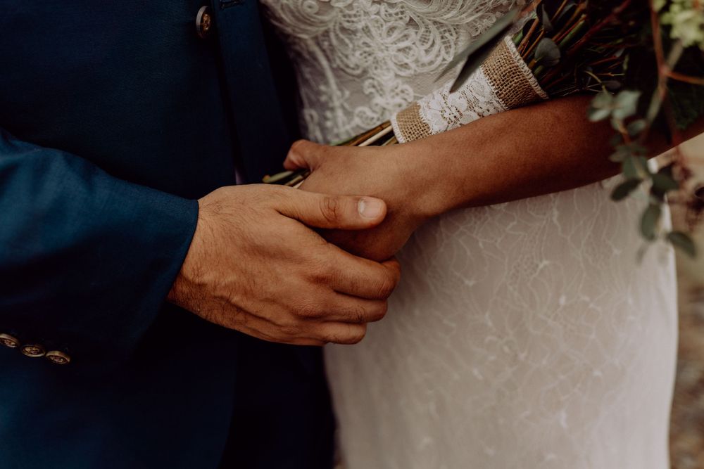 Close-up detail of hands clasped together with white wedding dress fabric in the background.