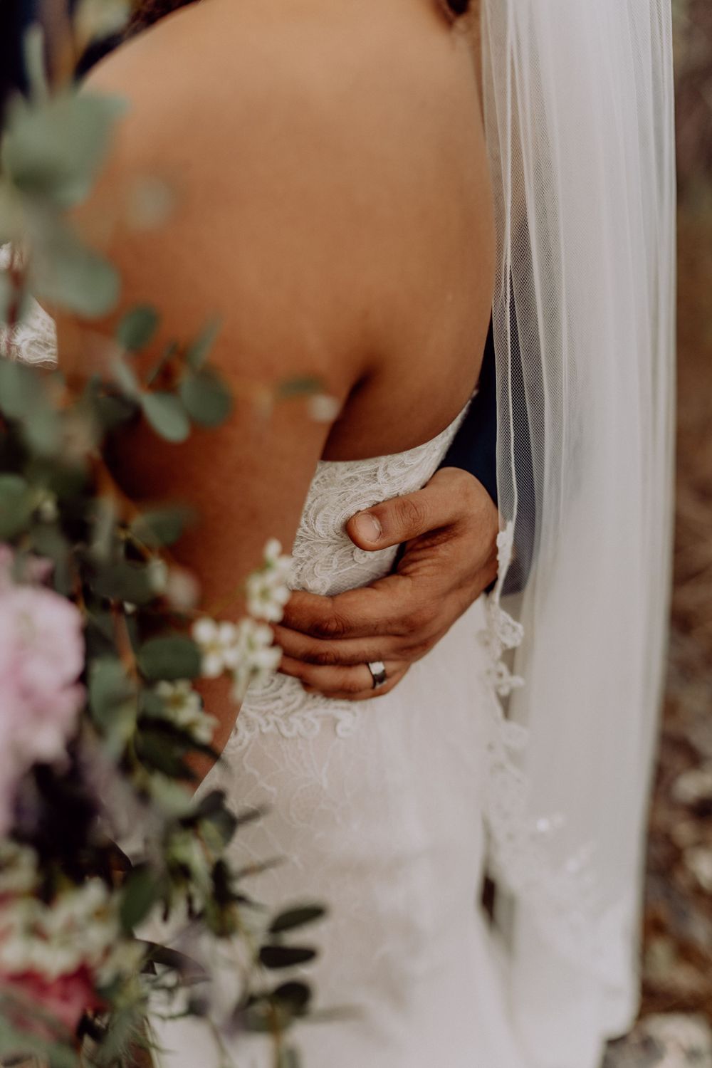Detail shot of lace wedding dress with delicate hand placement and floral accents.