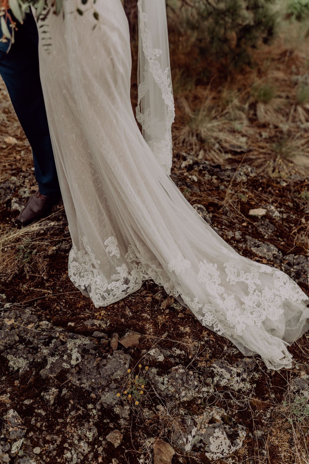 Elegant lace wedding dress train flows across rocky mountain terrain.
