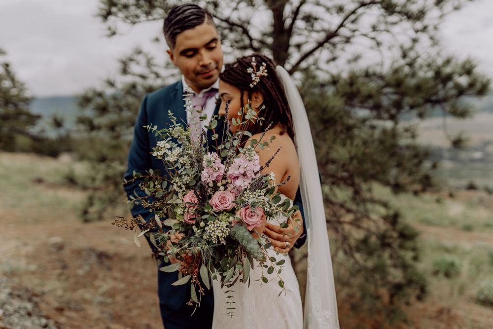 Couple shares tender moment while holding beautiful wildflower bouquet against mountain backdrop.