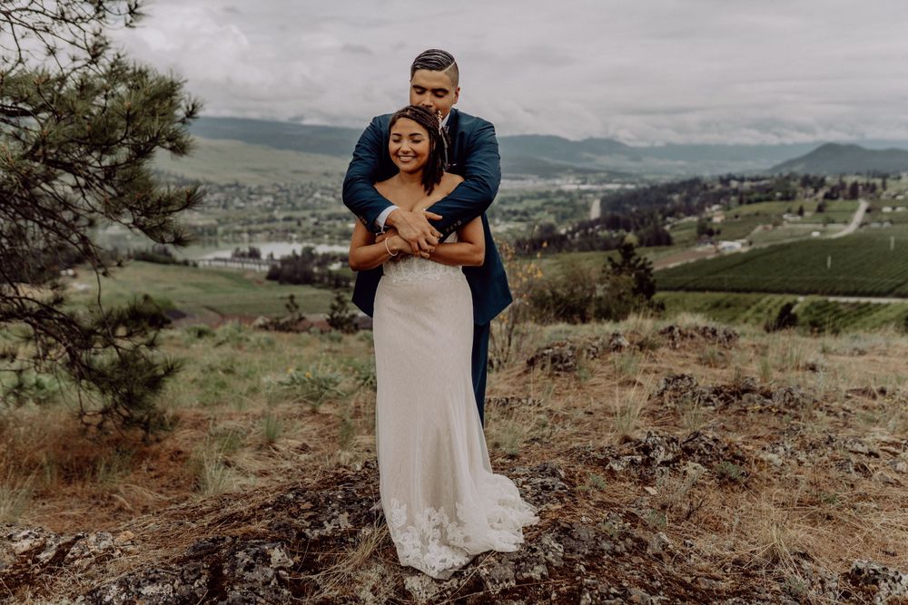 Romantic embrace captured on mountainside with sweeping valley views below.