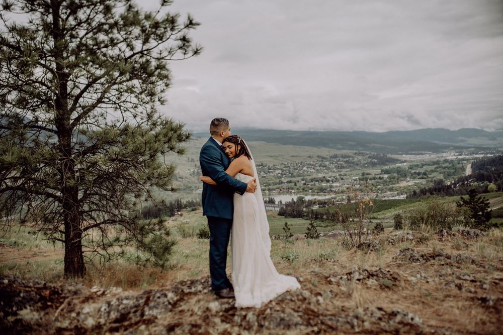 Couple shares intimate moment on mountainside with dramatic valley landscape behind.