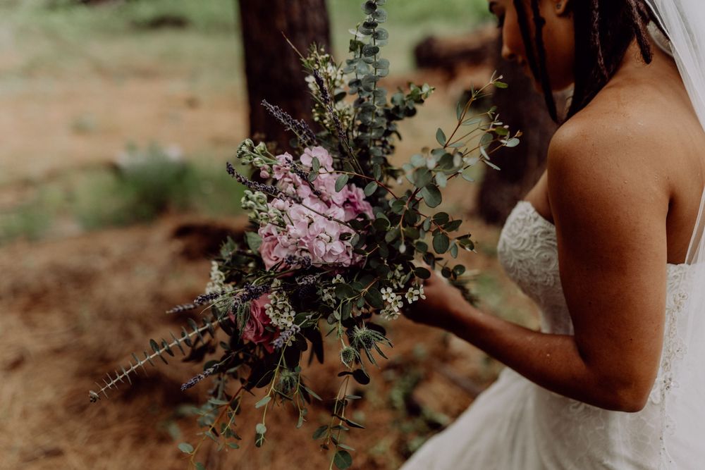 Wedding bouquet with pink flowers and greenery held against white dress.
