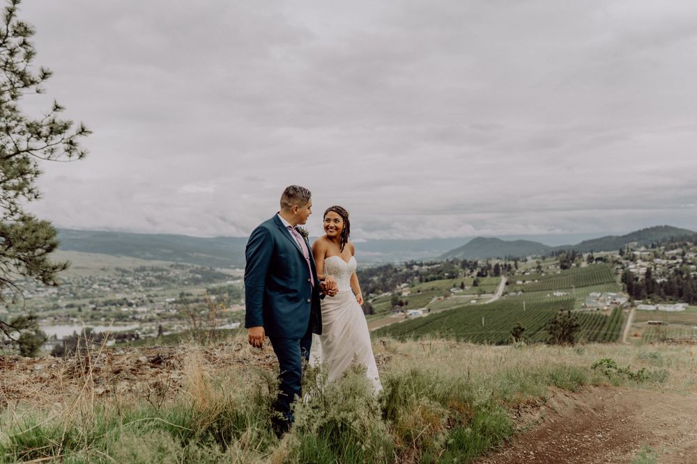 Newlyweds share an intimate moment on a grassy hillside with mountains and valley views.