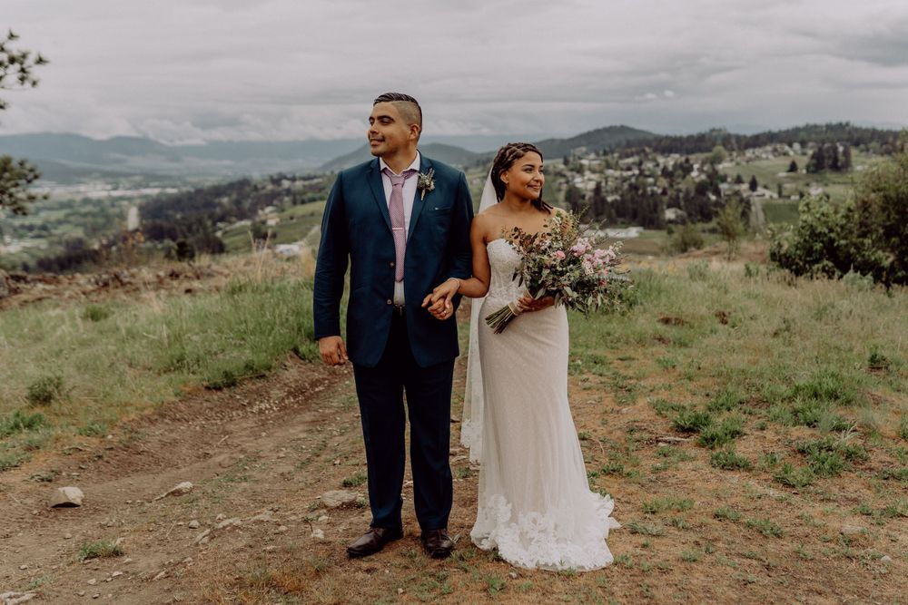 A wedding couple stands together on a mountain overlook with dramatic cloudy skies.