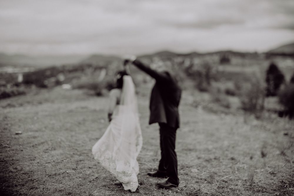 A black and white wedding photo showing a couple embracing on a hilltop.