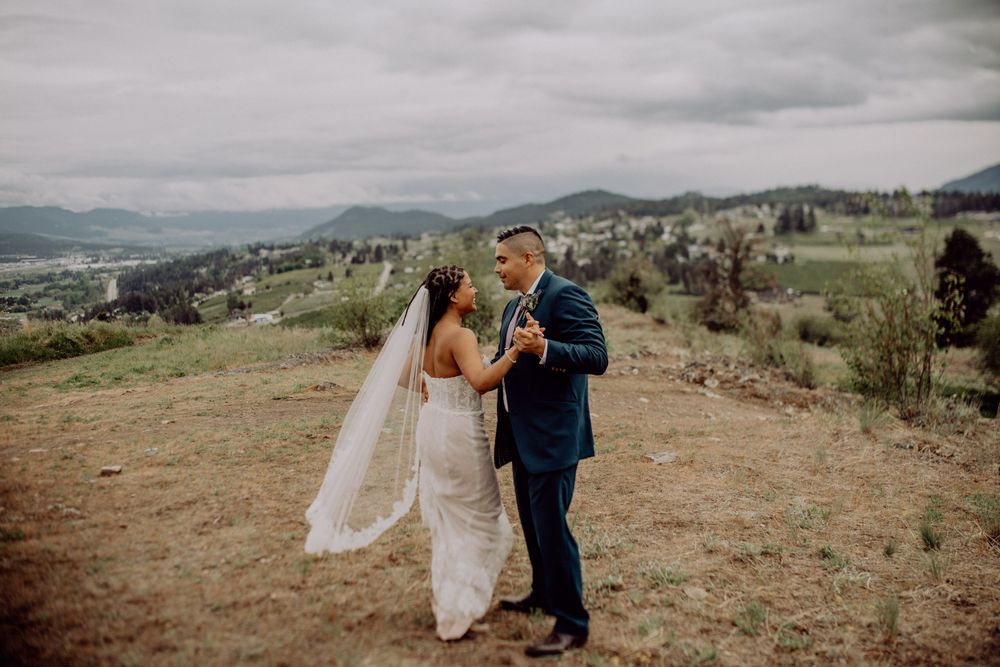 A wedding couple shares an intimate moment on a mountainside with cloudy skies and valley views.