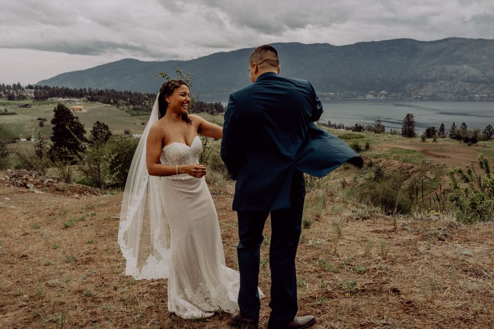 A couple shares a playful dance moment on a hilltop with mountain and lake views.